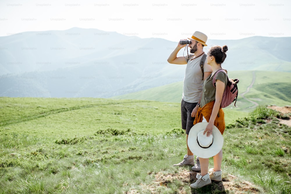 Couple enjoying beautiful landscape views, while traveling with backpacks in the mountains during the summer vacations