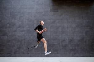 Vista lateral do belo esportista caucasiano em forma com perna artificial correndo do lado de fora.