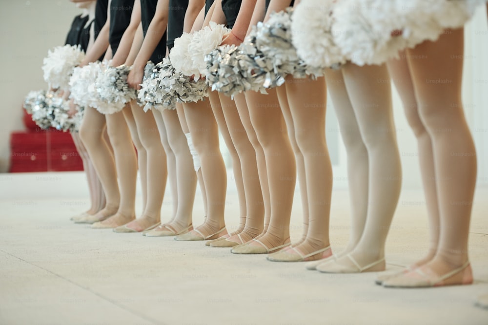 Gruppo di irriconoscibili ballerini di cheerleading in collant e scarpe da ballo in piedi con pompon in fila