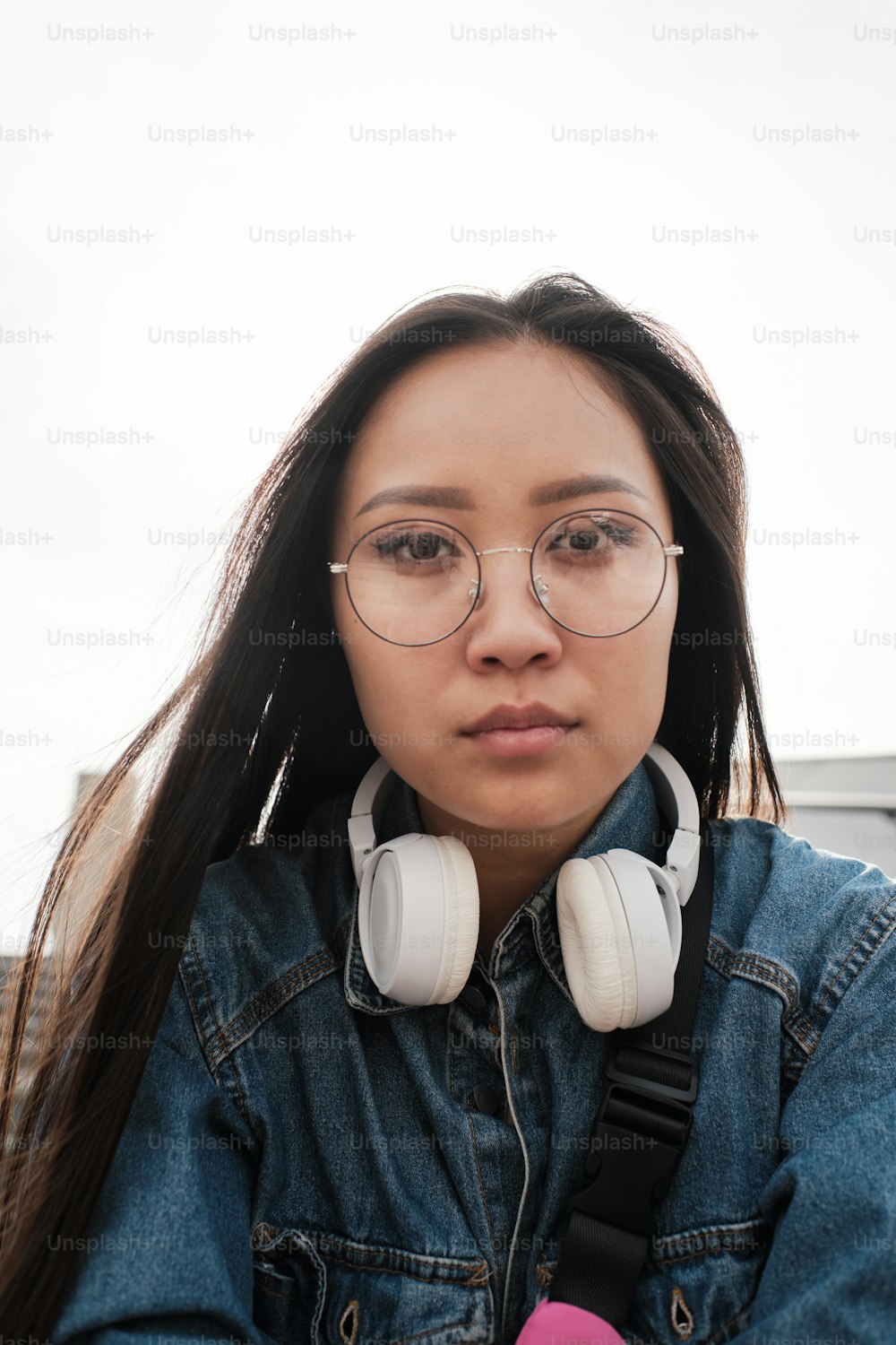 Portrait of an asian girl wearing glasses and headphones looking straight at the camera.