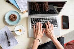 Überblick über menschliche Hände auf der Laptop-Tastatur während des Netzwerks durch Schreibtisch in häuslicher Umgebung