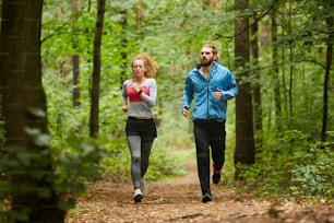 Giovane coppia sportiva che corre lungo il sentiero forestale o nel parco al mattino tra alberi verdi