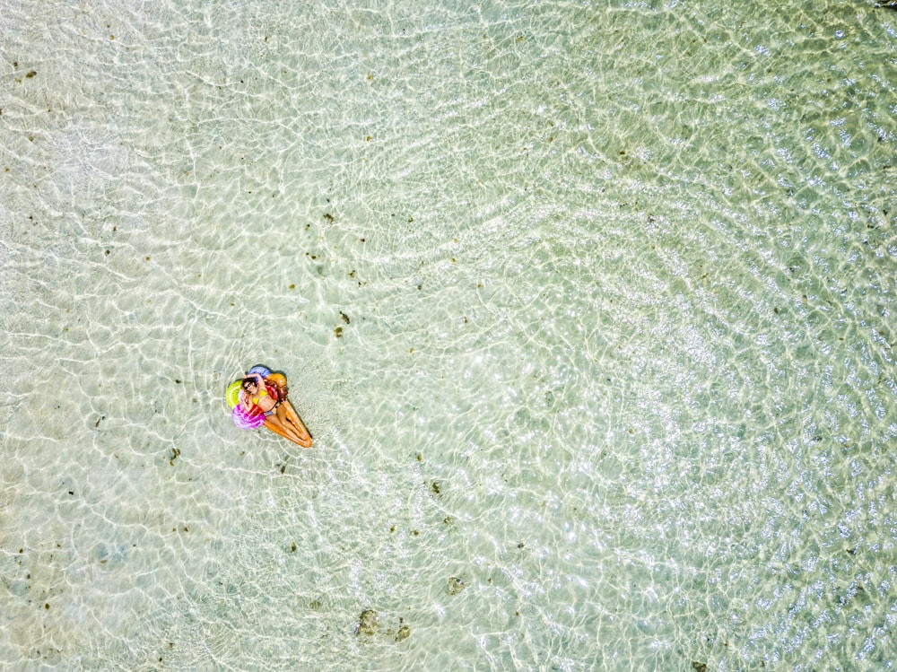 Aerial view of people in summer holiday vacation with beautiful girl on coloured trendy lilo relaxing and sunbathing on clear green ocean lagoon beach water
