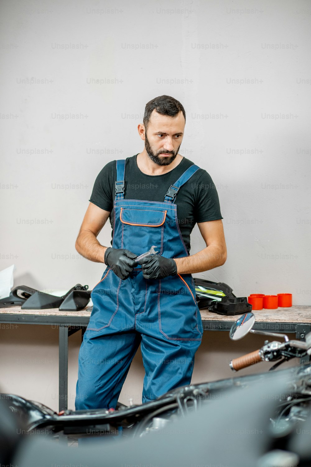 Retrato de un motociclista o reparador con mono de trabajo parado cerca de la motocicleta durante la reparación en el taller