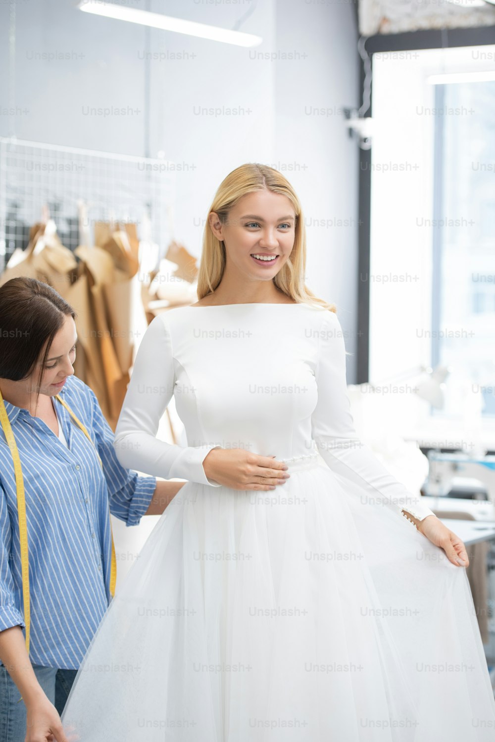 Happy blond-haired bride excited about wedding dress sewed by tailor in dressmaking studio