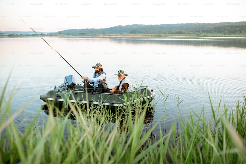 Avô com filho adulto pescando no barco inflável no lago com cana verde em primeiro plano no início da manhã