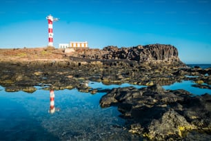 海岸に古典的な灯台と青いオセンと空を背景に美しい景色 – 観光のための旅行と休暇のコンセプト – 水への鏡の効果