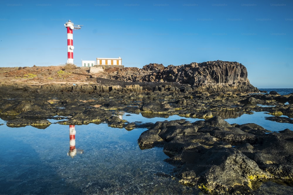 Beautiful scenic landscape with classic lighthouse on the coast and blue ocen and sky in background - concept of travel and vacation for tourism - mirror effect on the water
