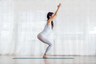 Young attractive yogi girl standing in Chair yoga pose. Yoga studio interior.