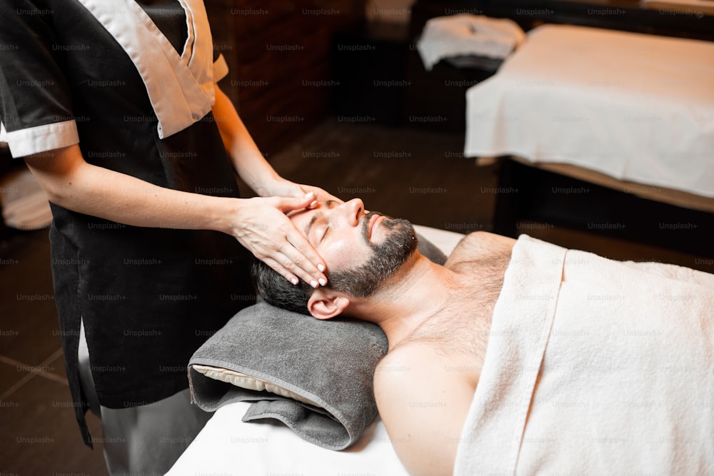 Hombre barbudo recibiendo un masaje facial, relajándose en el salón Spa, primer plano