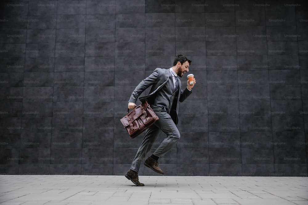 Young fashionable businessman running on the street. He is late for work.