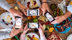 Persone che mangiano insieme scattando foto di cibo con lo smartphone da condividere sui social media - concetto di celebrazione - tavolo di legno e cibo misto sullo sfondo