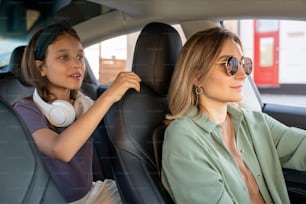 Linda niña con auriculares sosteniendo un asiento de cuero negro de su madre conduciendo un automóvil eléctrico