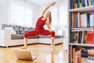 Smiling fit yoga instructor standing in goddess yoga posture and having online class. Home interior.