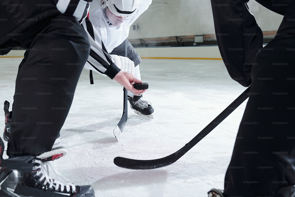 Un arbitre de hockey tenant la rondelle au-dessus de la patinoire tandis que deux rivaux avec des bâtons se penchent vers l’avant et attendent le moment pour être les premiers à la tirer
