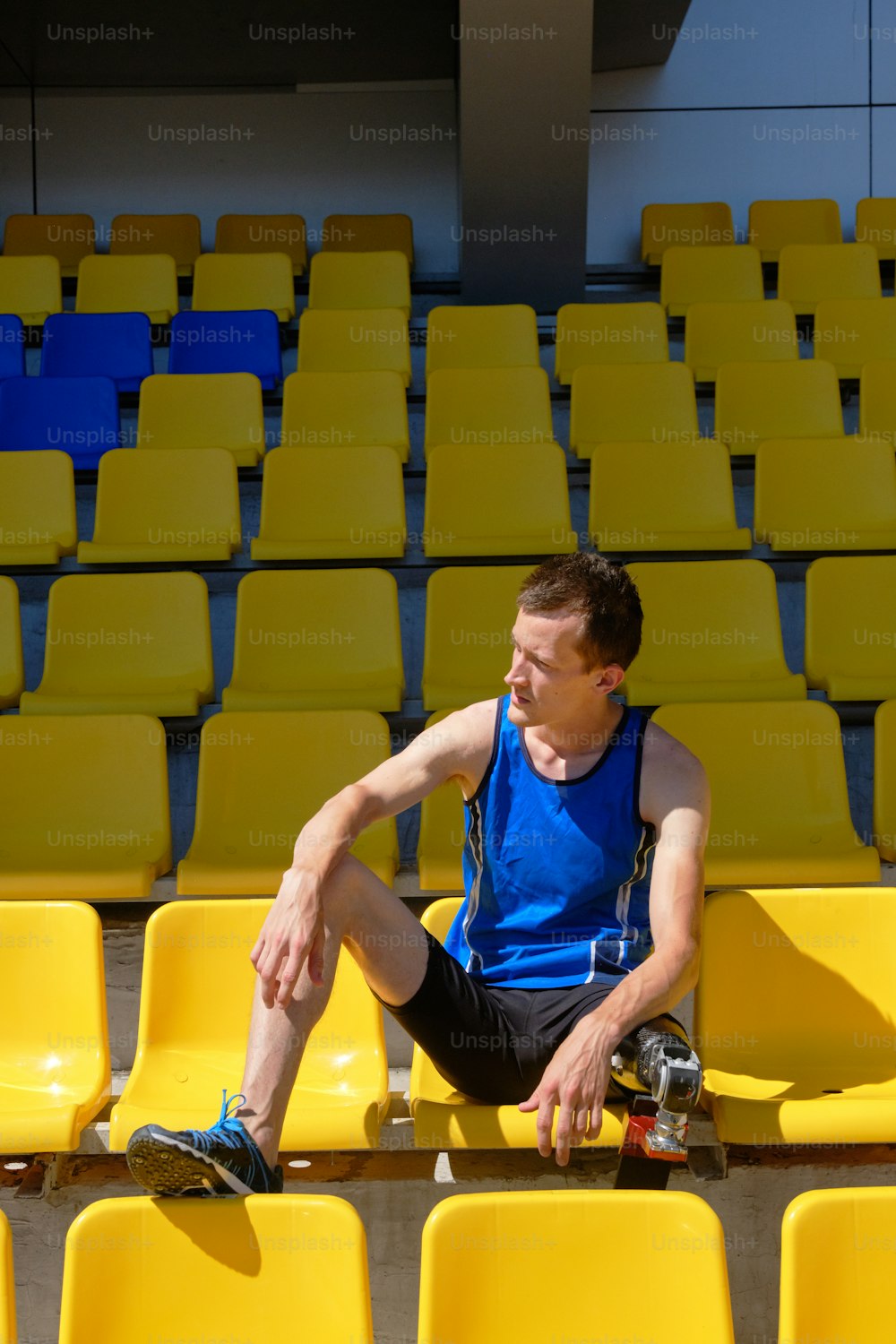 Portrait of adaptive athlete with prosthetic foot sitting on the empty stadium on sunny summer day. Real bodies, equal sport, disability recovery concept