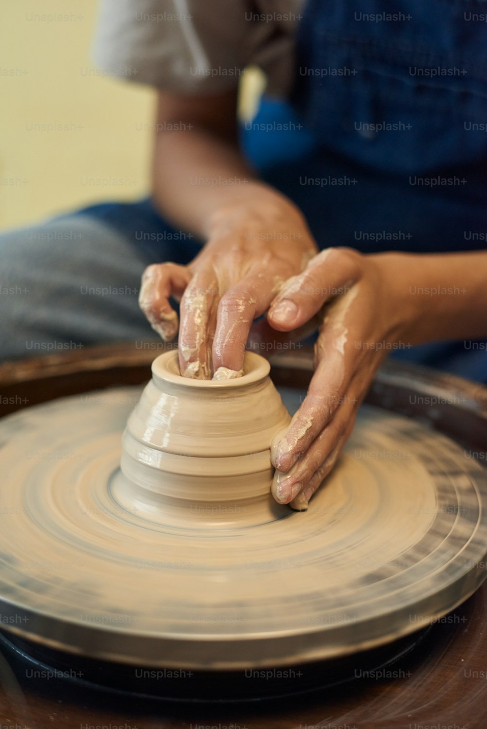 Primer plano de un alfarero irreconocible con paredes mojadas y sucias moldeando a mano de olla de barro en la rueda de cerámica