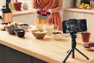 Young housewife with bowl of fresh strawberries giving masterclass of cooking smoothie