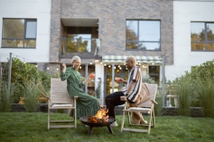 Multiracial couple drinking cocktails during home party in their garden. Burning fire for bbq. Concept of relationship. Modern domestic lifestyle. Black man and european girl enjoying time together