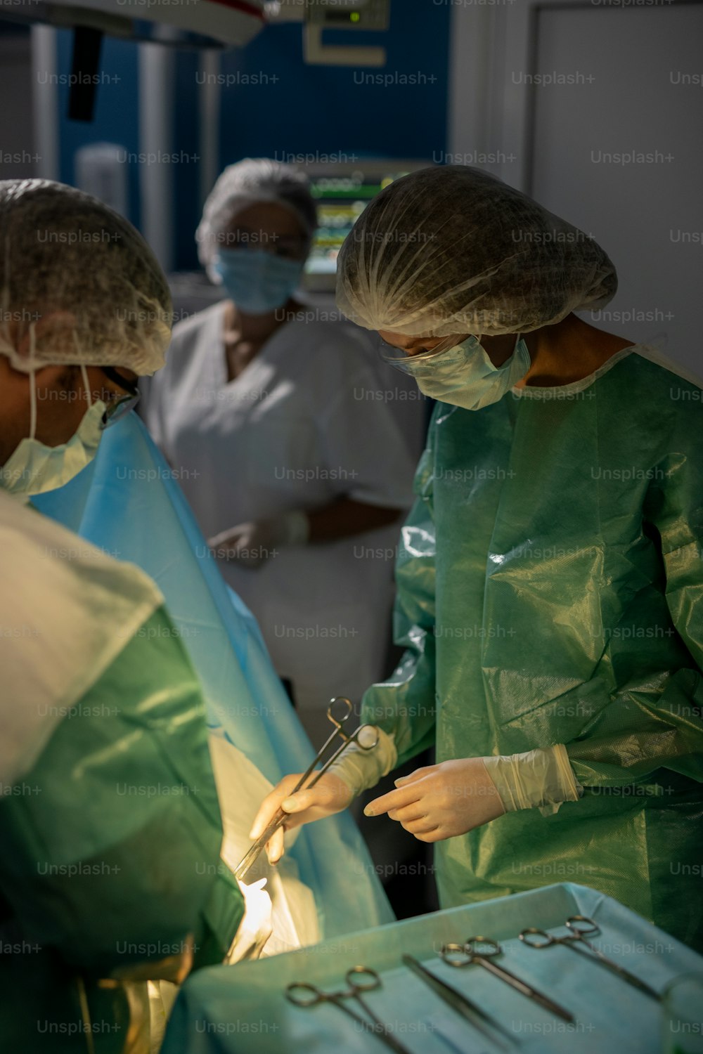 Contemporary surgeons in coveralls, protective masks, eyeglasses and gloves doing operation against their assistant in operating room