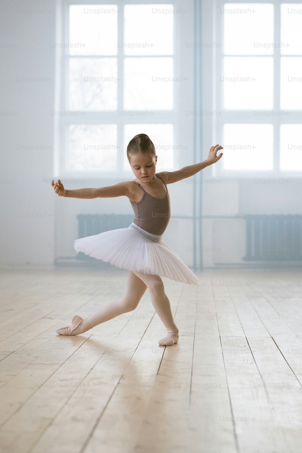 Little girl in tutu performing ballet dance alone in dance school