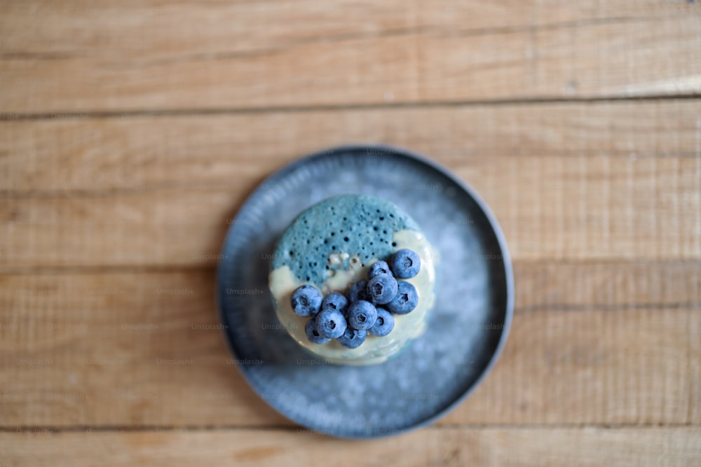 木のテーブルの上のビンテージプレートにブルーベリーとキャラメルのスースで飾られた青いアメリカのパンケーキ。自家製のおいしい食べ物。ざんげ節のお祝い。平面図。
