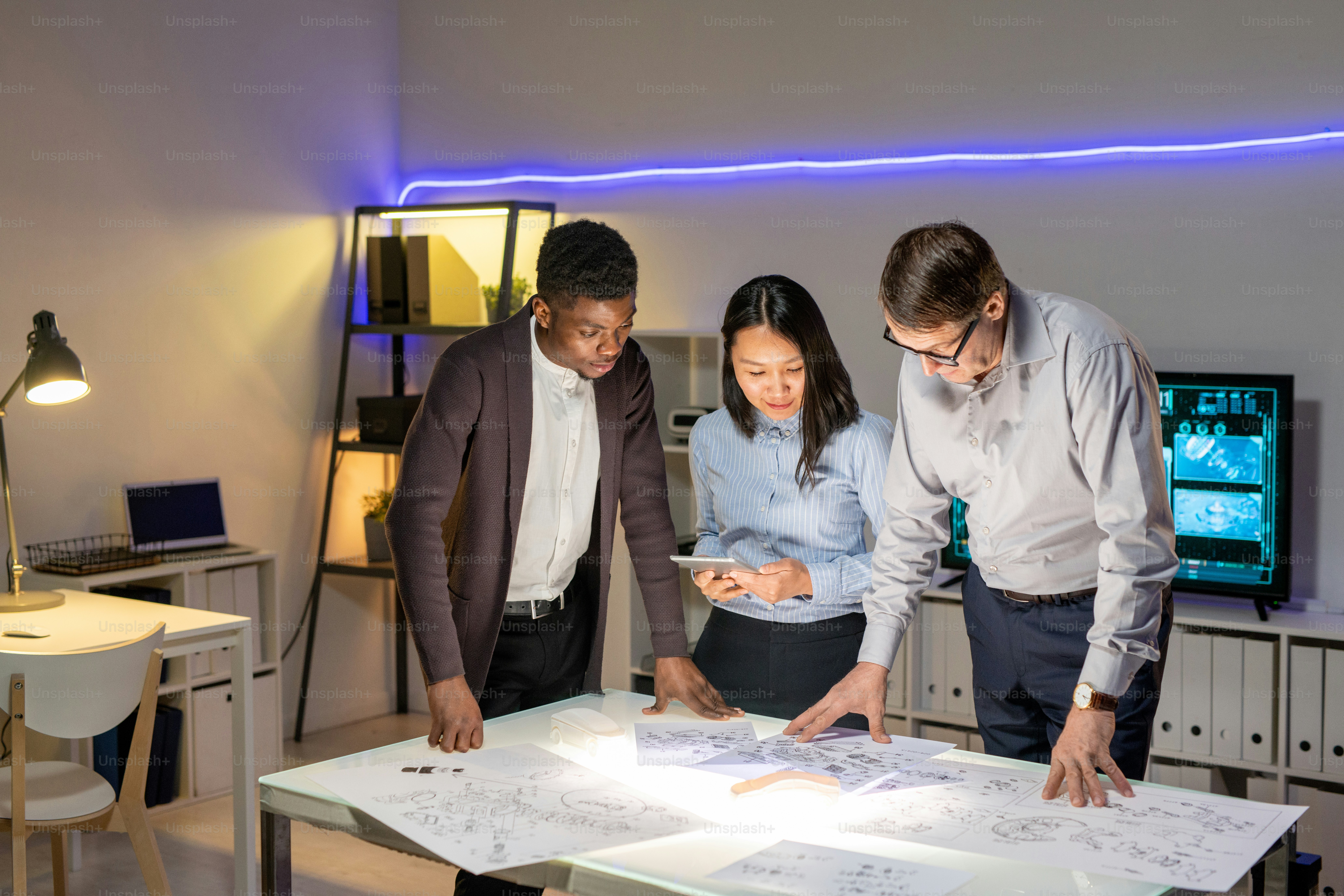 Team von multiethnischen Designern steht am Schreibtisch und diskutiert Automodellskizzen in modernem Büro