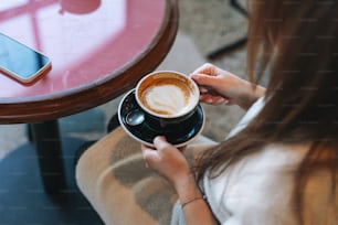 Jolie jeune femme brune souriante en robe blanche décontractée avec une tasse de café à la main dans le café