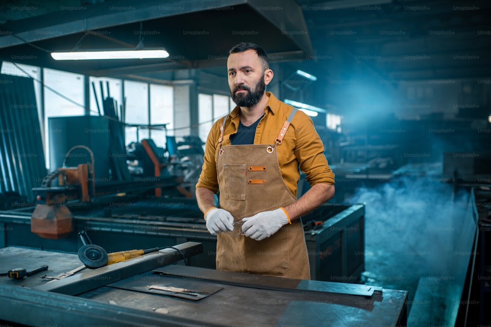 エプロンを着た金属産業の労働者が工場での作業の準備をしています。金属製品の製造におけるハンサムな職人。高品質の写真