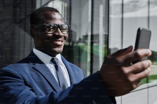 Retrato de hombre de negocios africano usando un teléfono inteligente al aire libre. Navegación, chat, videoconferencia, concepto de trabajo remoto