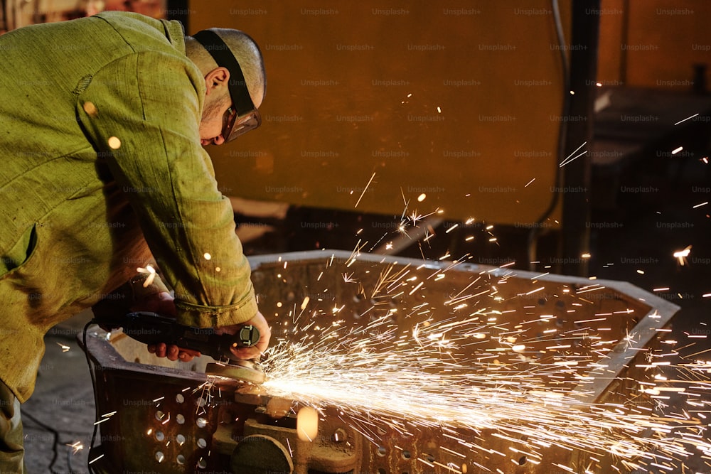 Ouvrier en vêtements de travail de protection travaillant avec le soudage de l’acier dans un atelier d’assemblage