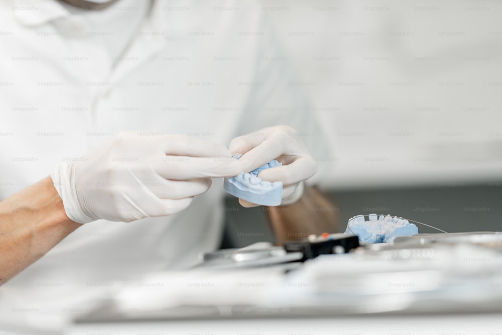 Zahntechniker, der mit einem Zahnmodell arbeitet und im Labor ein Zahnspangensystem für die kieferorthopädische Behandlung anprobiert. Nahaufnahme. Hochwertiges Foto