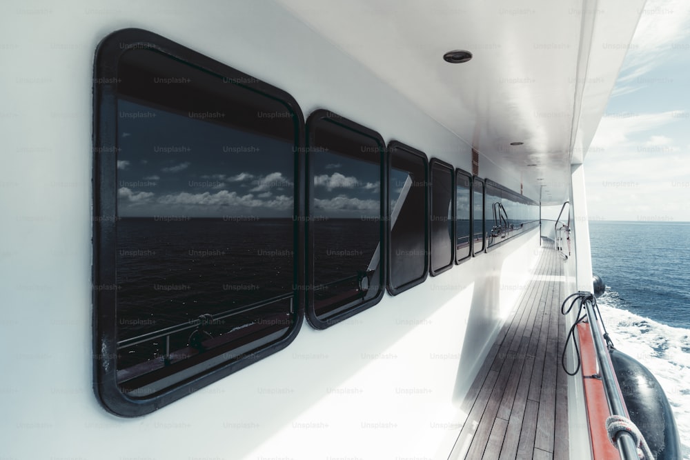 Wide-angle view of the side-deck of a luxurious white safari yacht with a row of windows of the deckhouse wooden floor of the ways and the waterscape astern with a blue ocean water