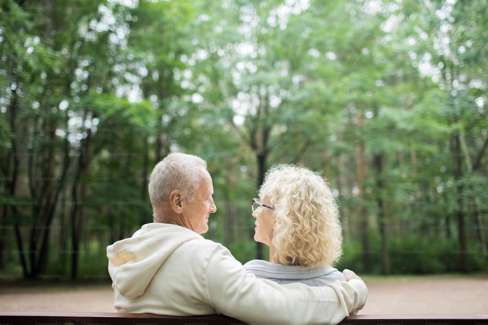 Rear view of aged spouses looking at each other during talk while sitting in park