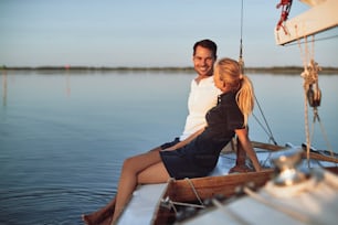 Smiling young husband and wife talking together while sitting on the deck of their boat enjoying an afternoon sailing
