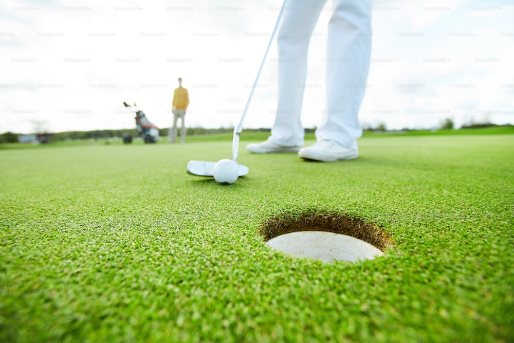 Jogador de golfe segurando o taco perto da bola antes de acertá-la enquanto mira no buraco