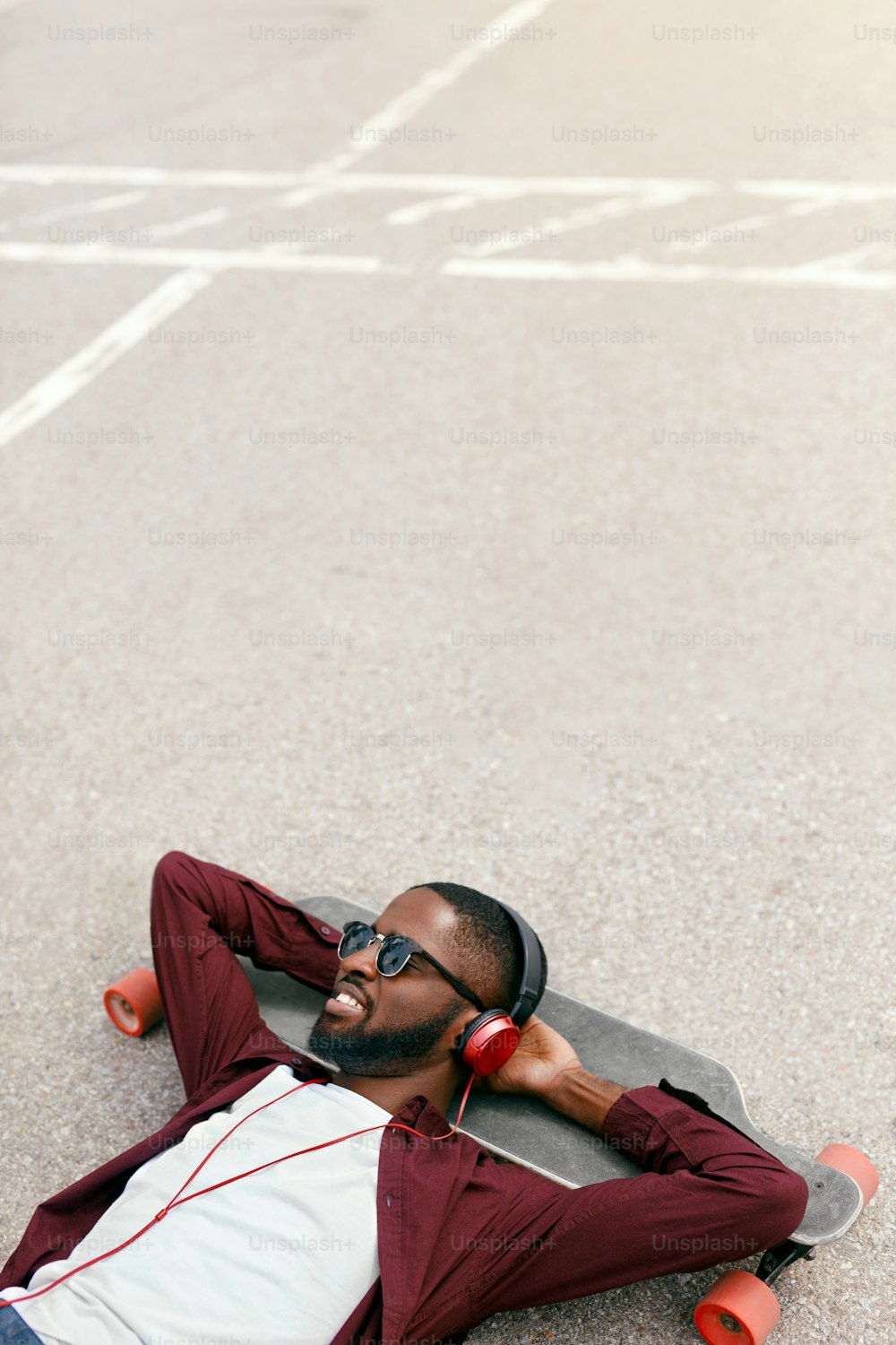 Fashion. Black Man Listening Music In Headphones On Street, Lying On Longboard. High Resolution