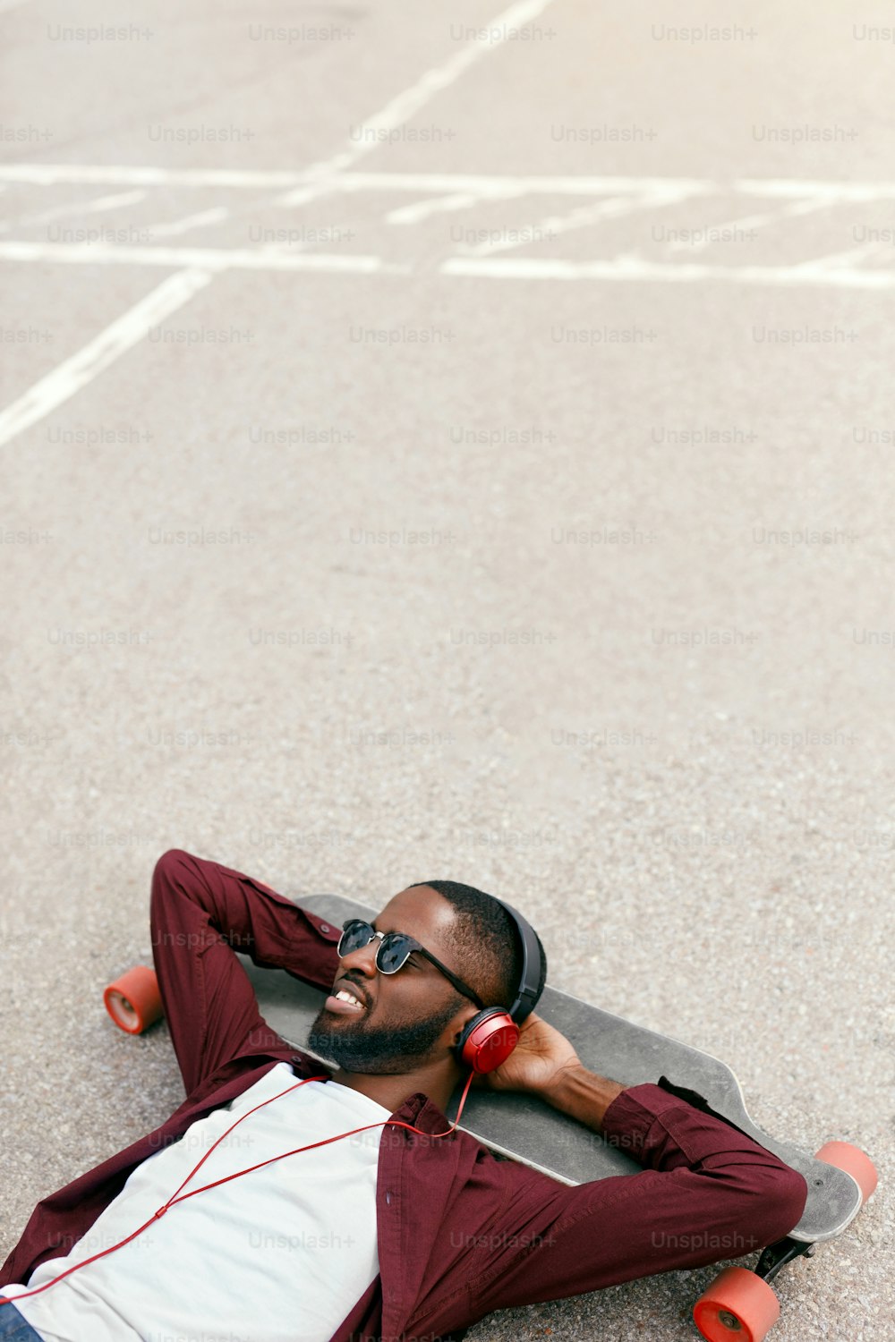 Mode. Homme noir écoutant de la musique dans des écouteurs dans la rue, allongé sur du longboard. Haute résolution
