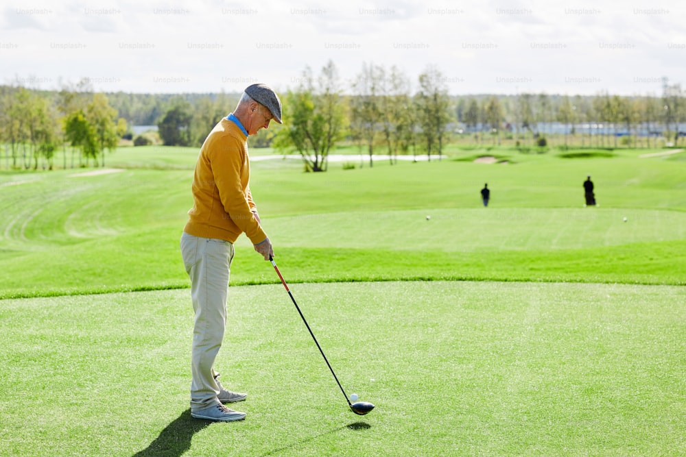 Homme âgé en tenue décontractée debout au milieu du champ vert et allant frapper une balle de golf