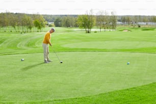 ゴルフクラブを持つ成熟した男性が、遊び場の緑の芝生の上に立ったままボールを打つ