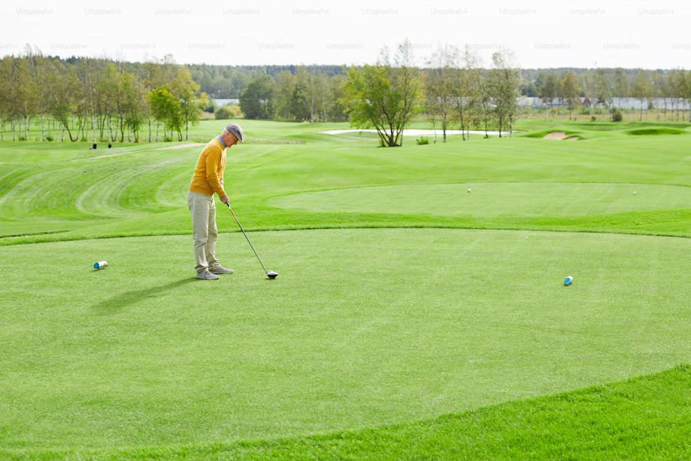 ゴルフクラブを持つ成熟した男性が、遊び場の緑の芝生の上に立ったままボールを打つ