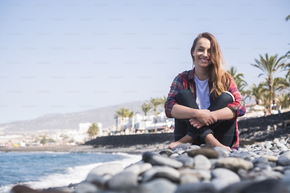 young smile beautiful lady sitting on the rocks near the ocean and the waves to enjoy the outdoor leisure activity on summer vacation. beautiful woman with modern casual clothes