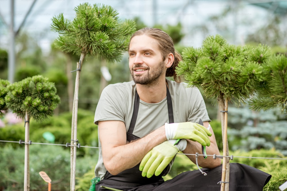 Portrait of a handsome gardener in uniform in the greenhouse
