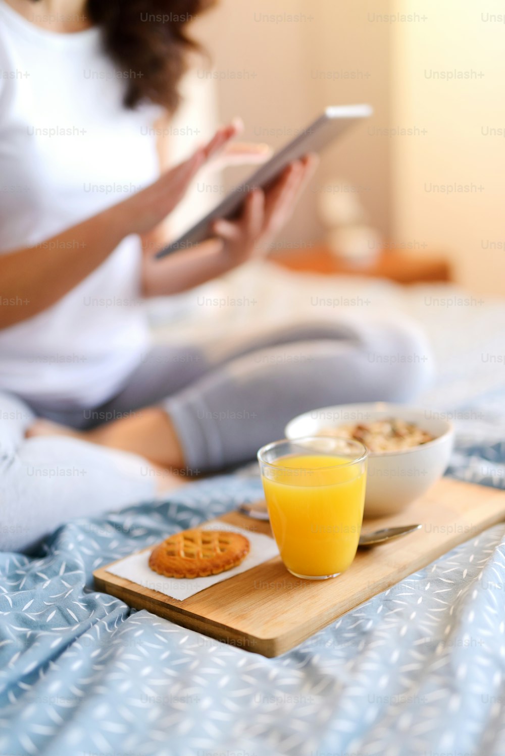 ベッドでの健康的な朝の朝食。タブレットを持つ女性のぼかした姿。