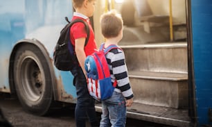 Two sweet boys with backpacks are entering a school bus.