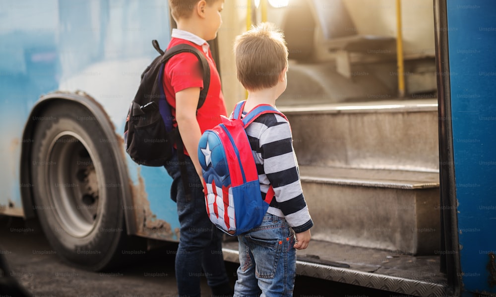 Dos niños dulces con mochilas están entrando en un autobús escolar.