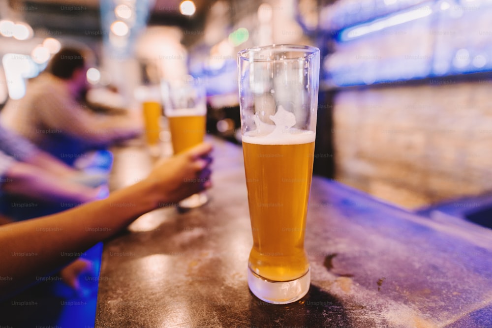 テーブルの上に立っているビールのグラスに選択的に焦点を合わせます。バックグラウンドでビールを飲む人々。
