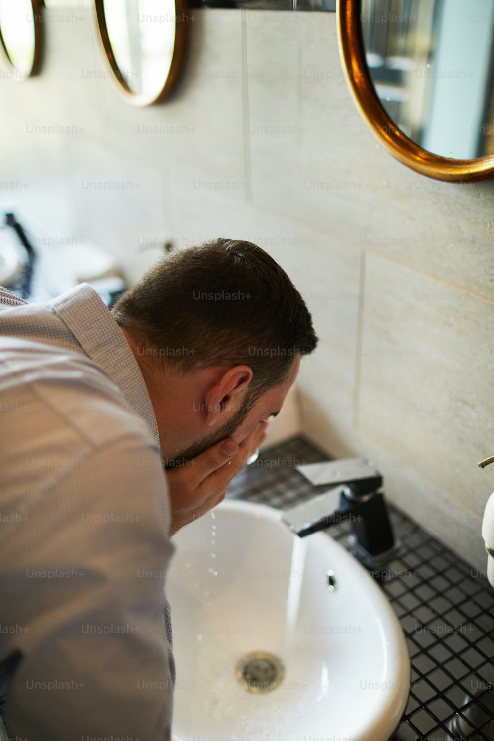 Tired or sleepy businessman refreshing with cool water over sink in bathroom of airport