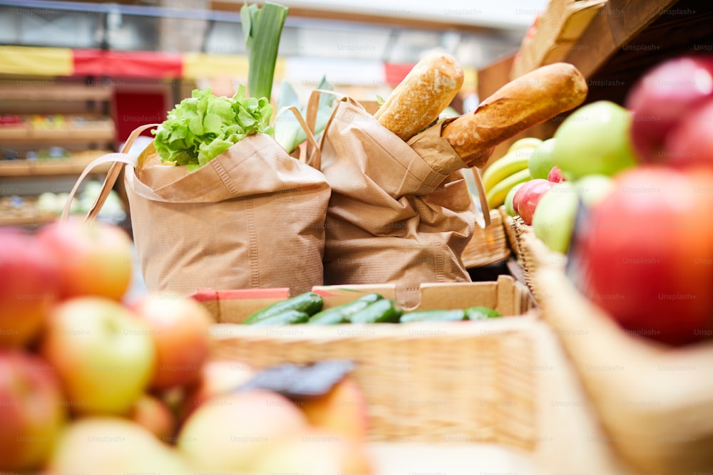 Close-up of shopping bags full of fresh products such like bread vegetables and greens on counter