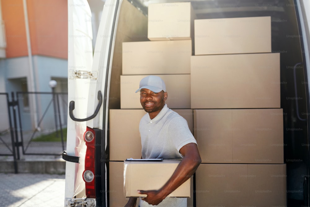 Serviço de Entrega de Courier. Retrato do homem negro entregando pacote perto do carro com caixas ao ar livre. Alta Resolução